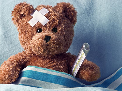 a brown teddy sits in bed with a plaster on its head