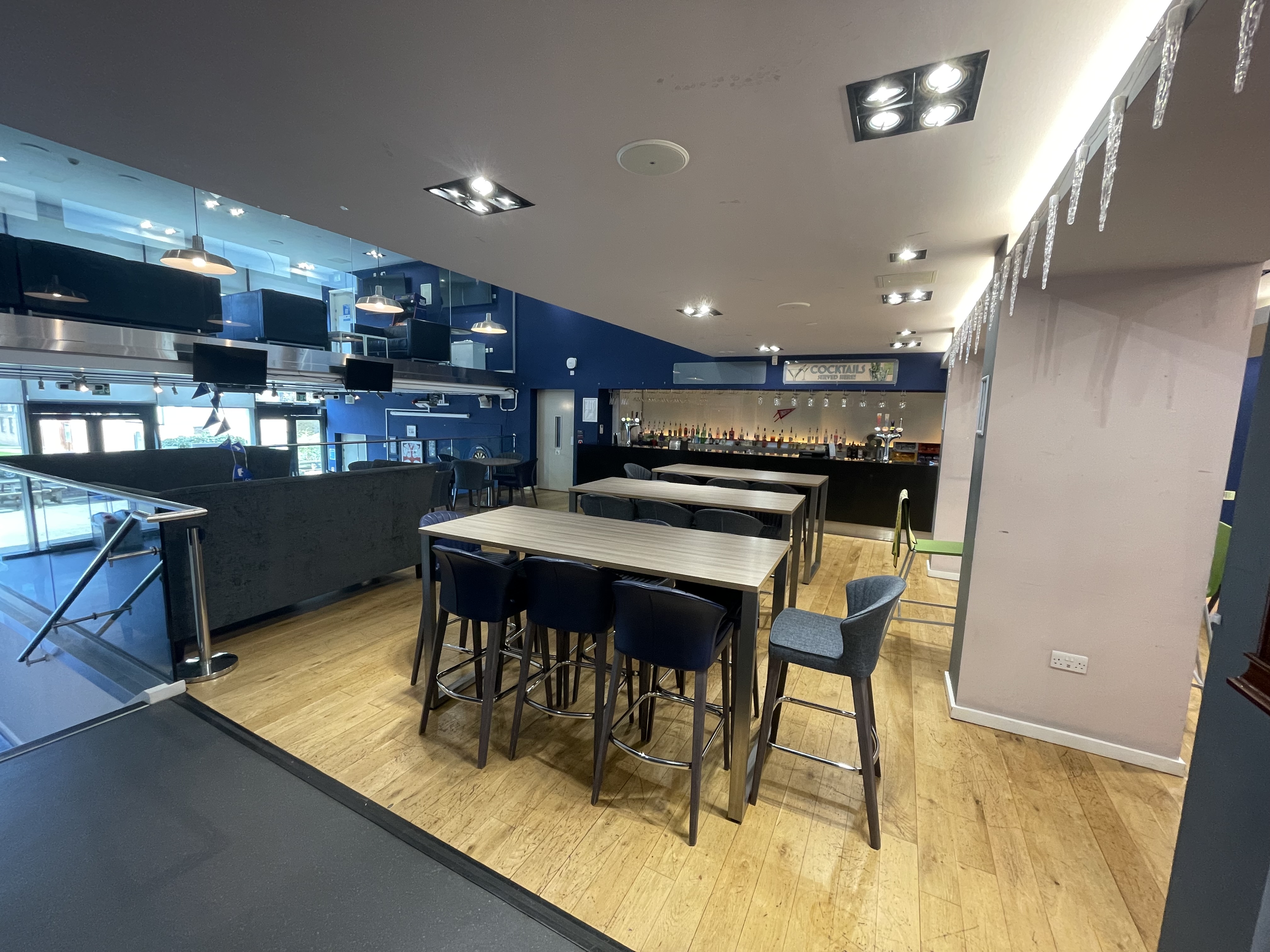 Grizedale bar, a college bar at Lancaster University campus. The bar area is located at the back, with blue bar stools and tables in front.