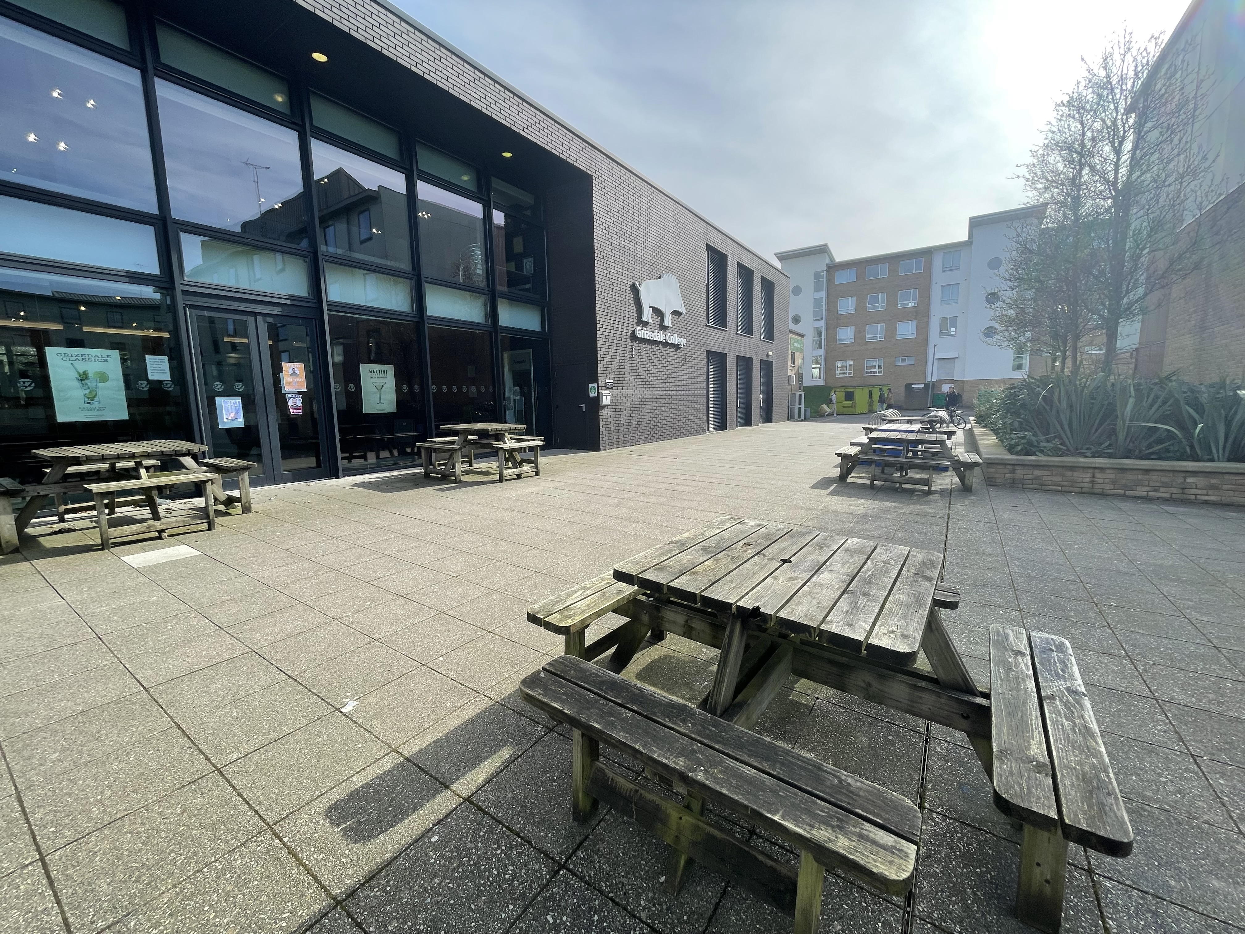Outside the Grizedale College building, seating areas and benches are in front.
