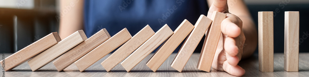 Blocks arrange like dominoes. They are falling over each other, but a hand stops the fall