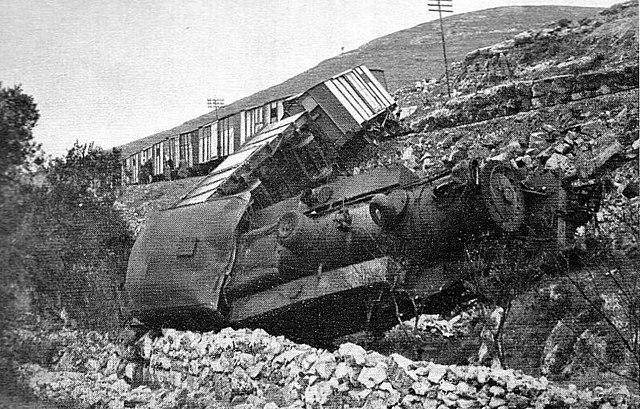 A black and white photo of a derailed train and rubble in the foreground.