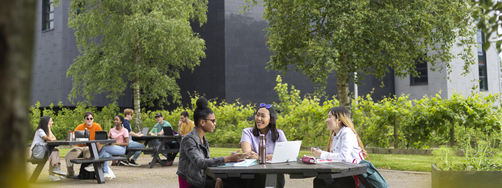 Students sat outside at a table with a modern building in the background.
