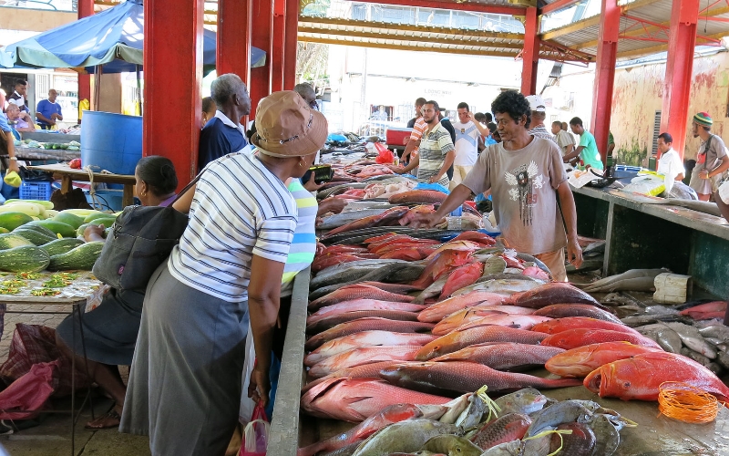 Customers and retailers around fresh fish laid out on tables in a tropical fish market